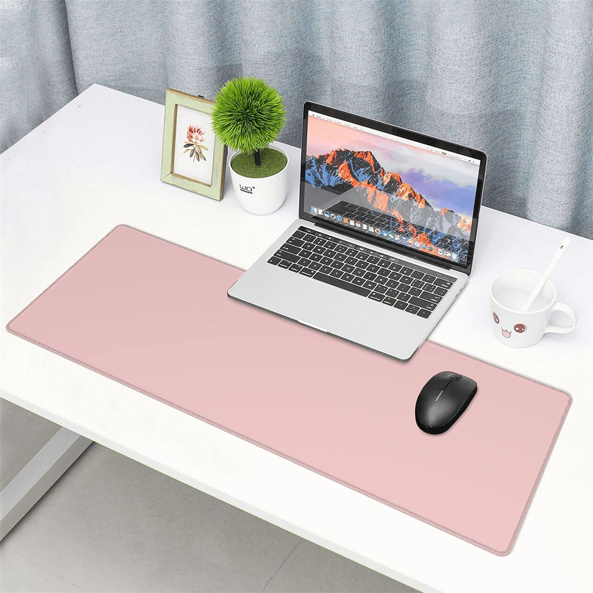 Rosa Mauspad auf einem weißen Schreibtisch. Ein Laptop, eine Maus, ein gerahmtes Bild und eine Tasse befinden sich auf dem Schreibtisch.