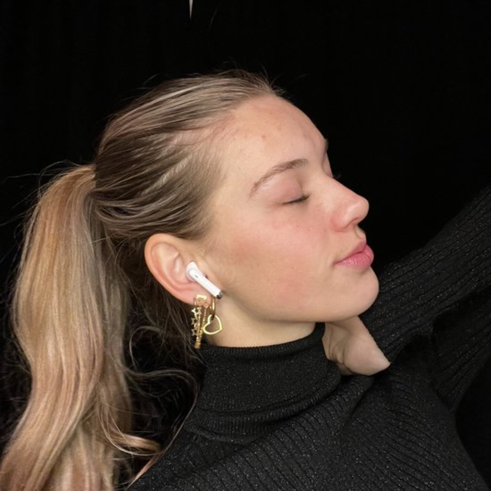 Frau mit Pferdeschwanz, die Ohrringe mit Airpods trägt. Schwarzer Rollkragen. Schwarzer Hintergrund.