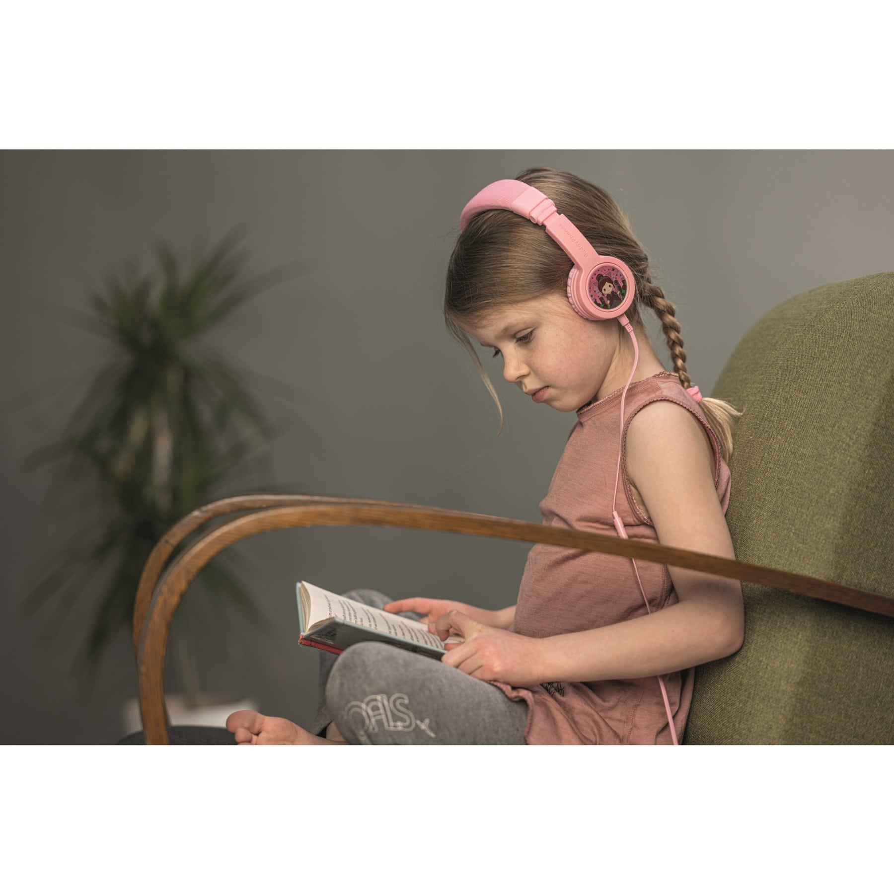 Una ragazza con le trecce che indossa delle cuffie rosa legge un libro.