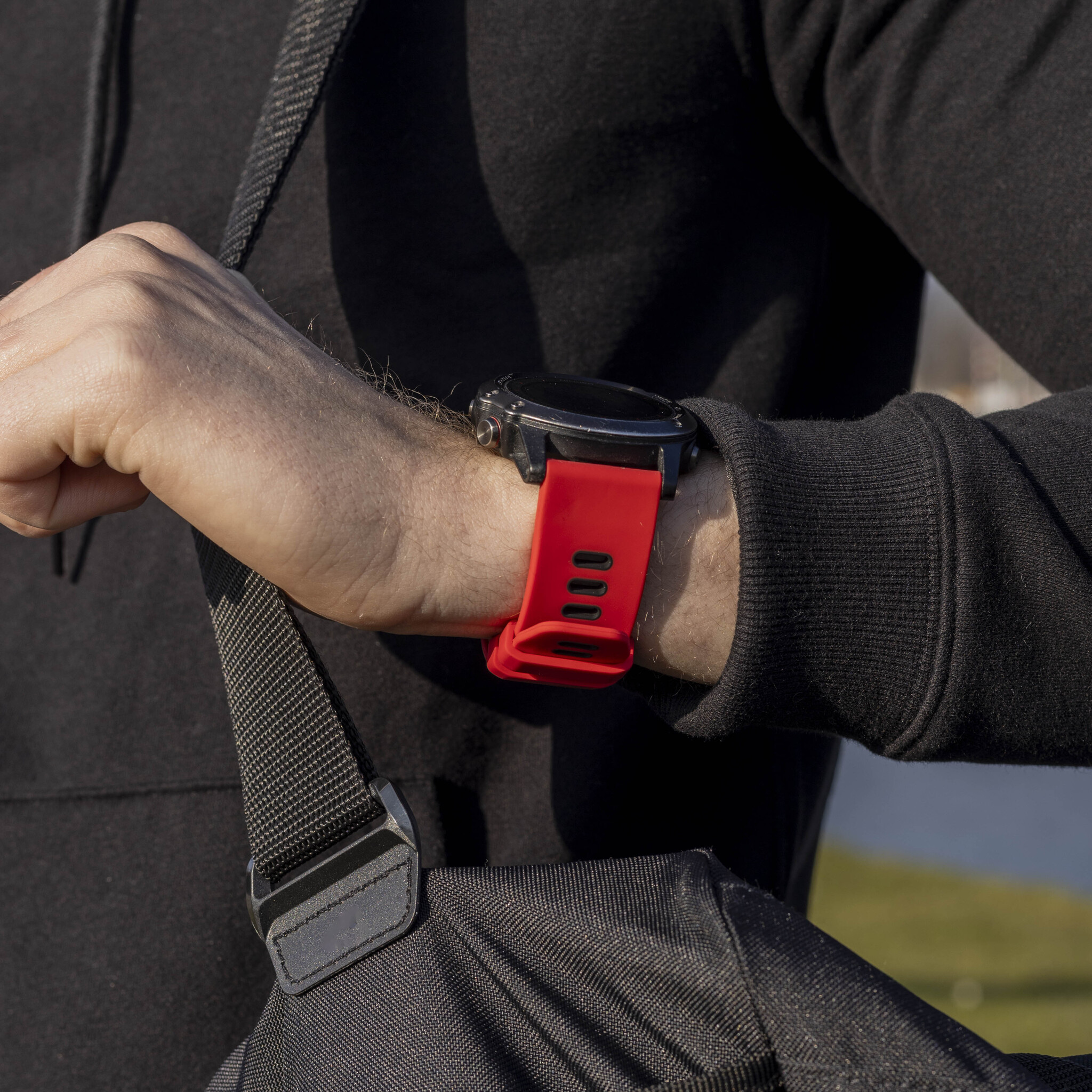 Eine Person mit einer schwarzen Smartwatch mit rotem Armband und einer schwarzen Tasche.