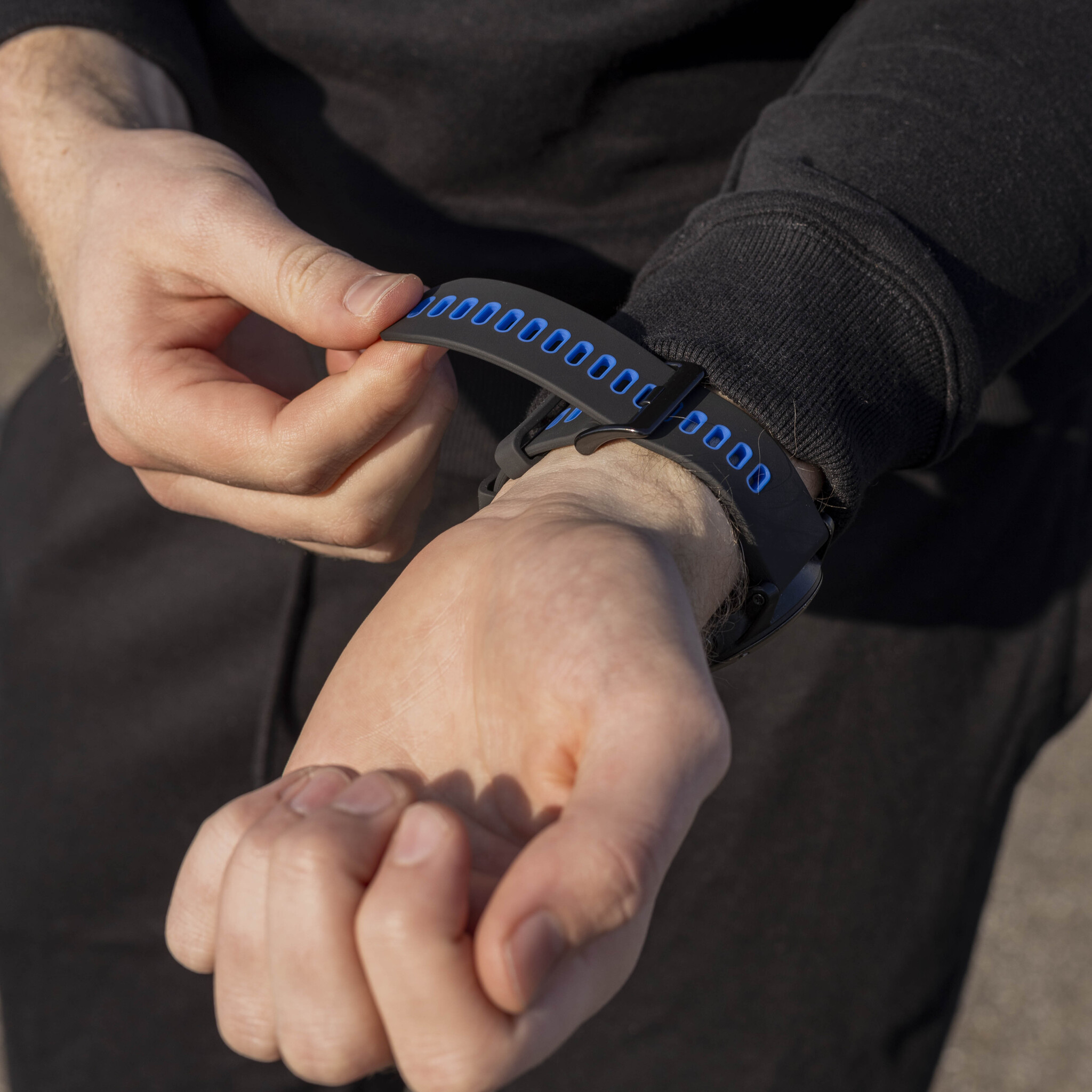 Person befestigt ein schwarzes Smartwatch-Armband. Das Armband hat ein blaues Muster mit Zahlen.