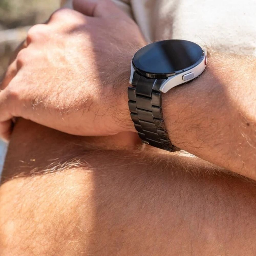 Handgelenk einer Person mit silberner Smartwatch und schwarzem Metallband.