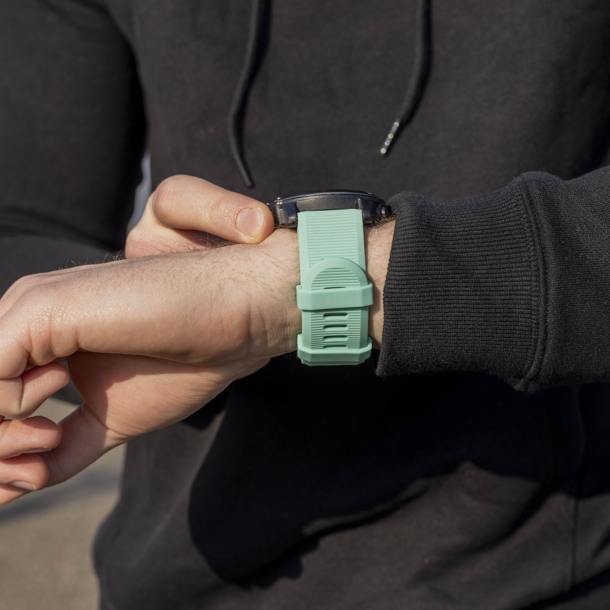 Eine Person, die ihre mintgrüne Uhr mit hellgrünem Armband überprüft.