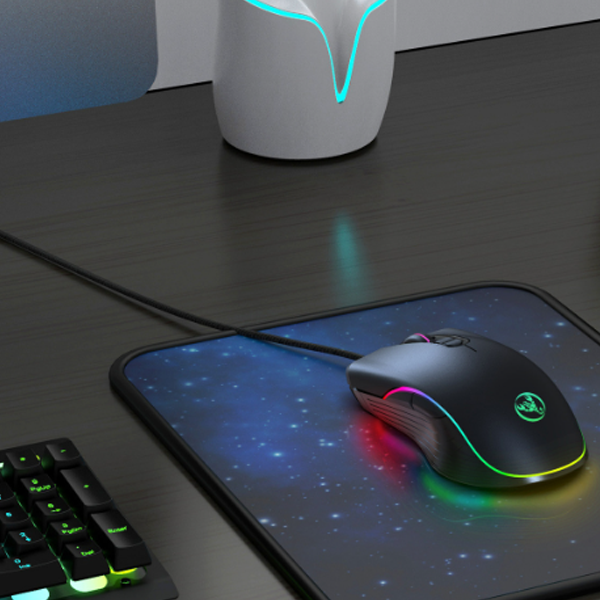 Eine schwarze Gaming-Maus auf einem Mauspad mit farbenfrohem Design, neben einer Tastatur und einem leuchtenden Licht.