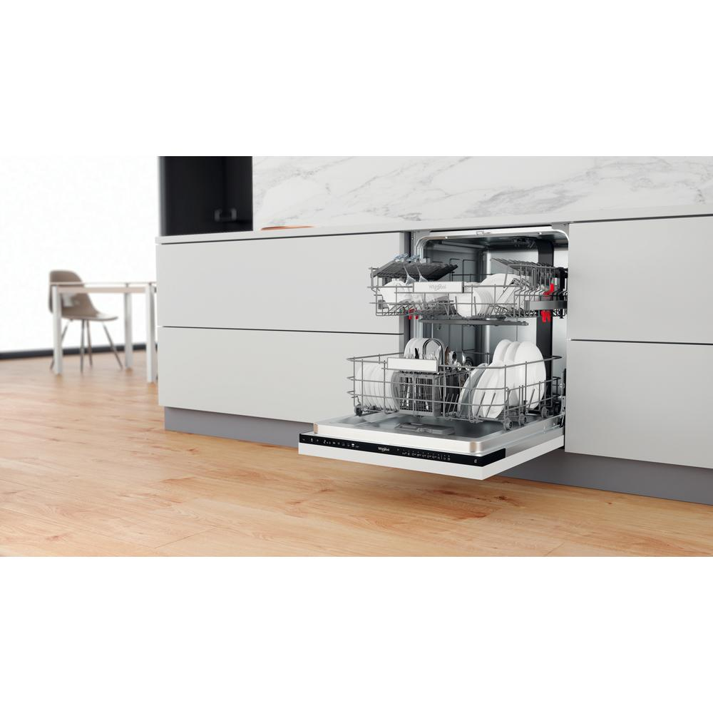 Biała zmywarka z otwartymi drzwiami, wypełniona naczyniami i szklankami. Scena w kuchni z drewnianą podłogą.