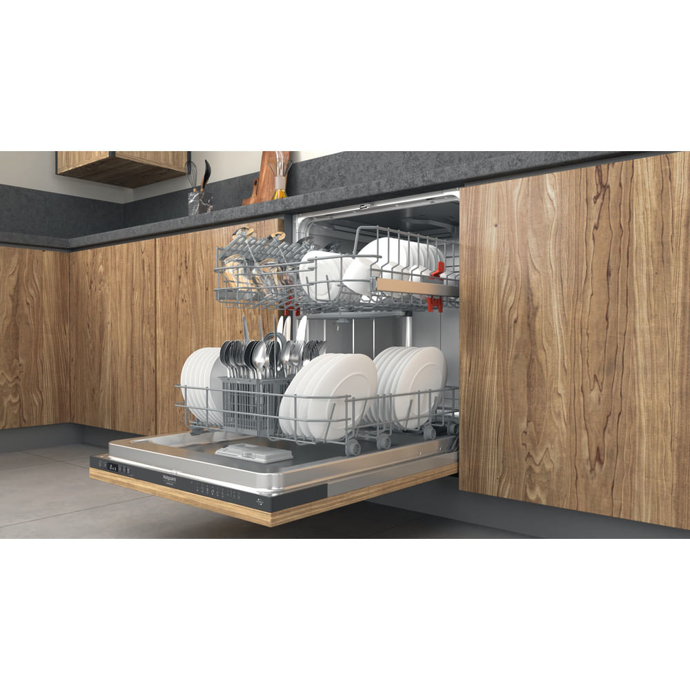 Lavastoviglie Hotpoint parzialmente aperta caricata con piatti bianchi, argenteria e pentole in una cucina moderna.