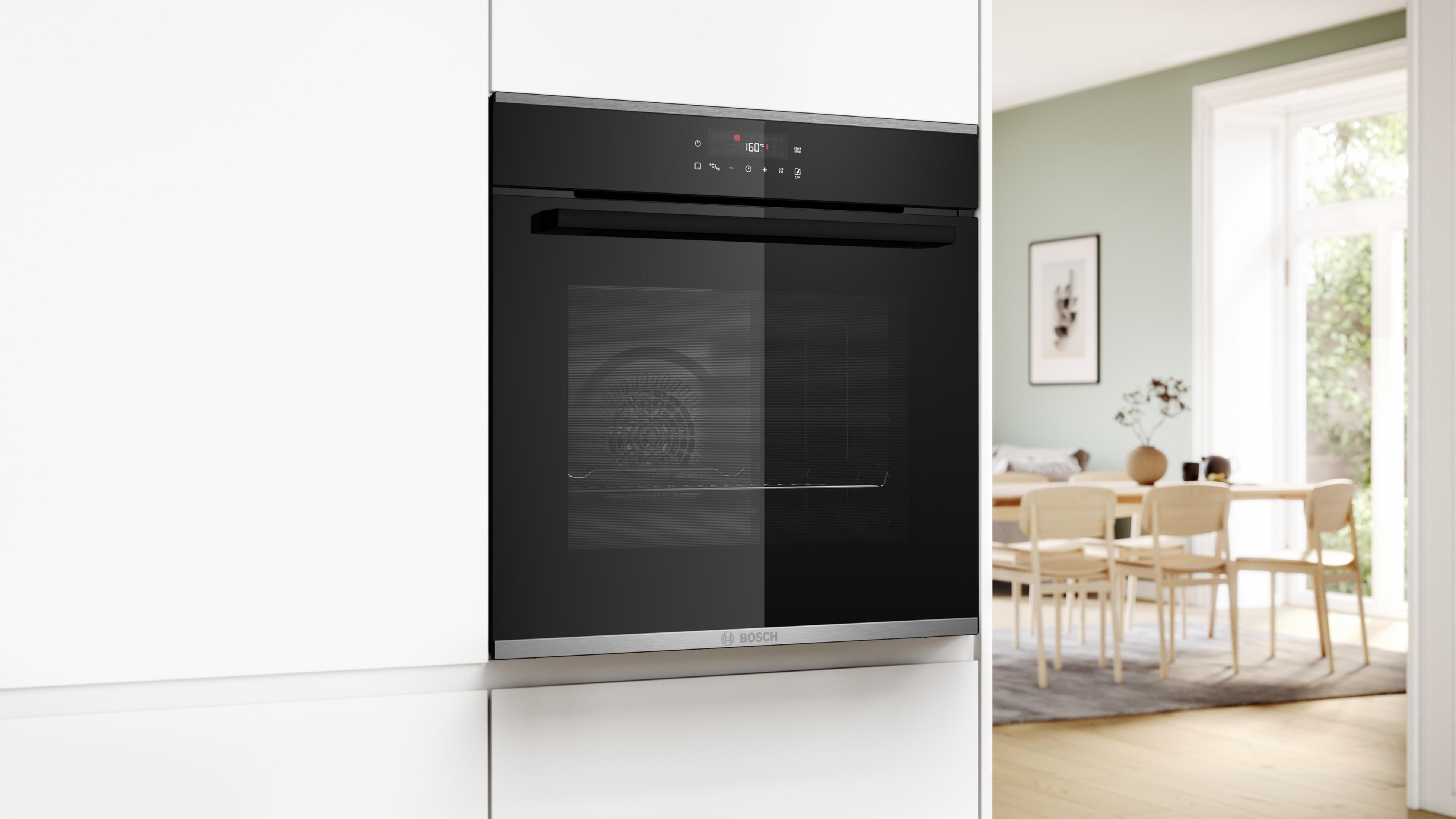 Forno nero integrato in un mobile bianco. Stanza con tavolo da pranzo sullo sfondo.