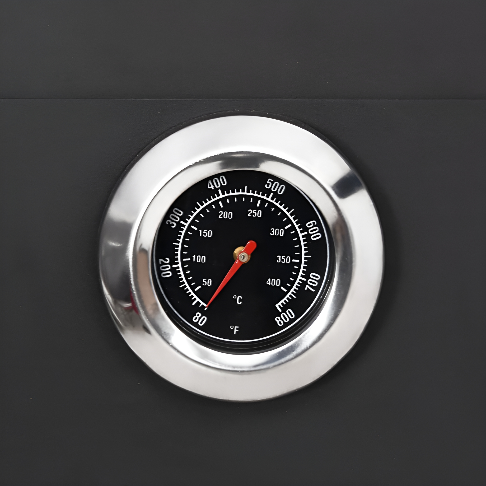 Ein Thermometer mit schwarzem Zifferblatt und roter Nadel, in einem Metallrahmen.