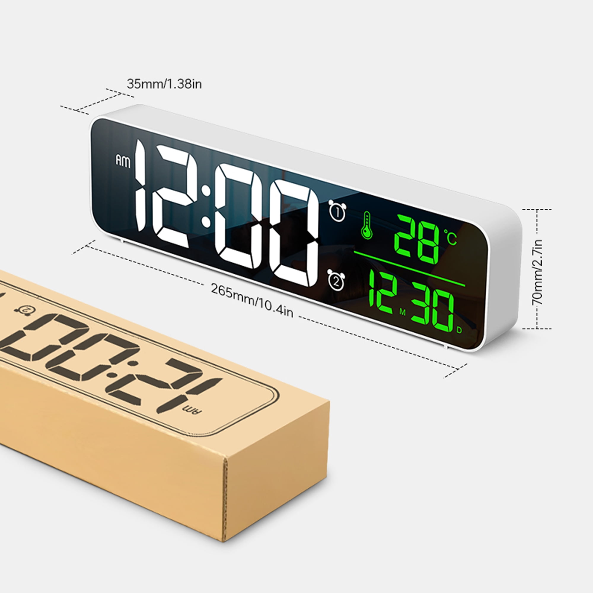 Eine Digitaluhr mit weißem Rahmen zeigt Zeit und Temperatur an. Daneben liegt ein Karton.
