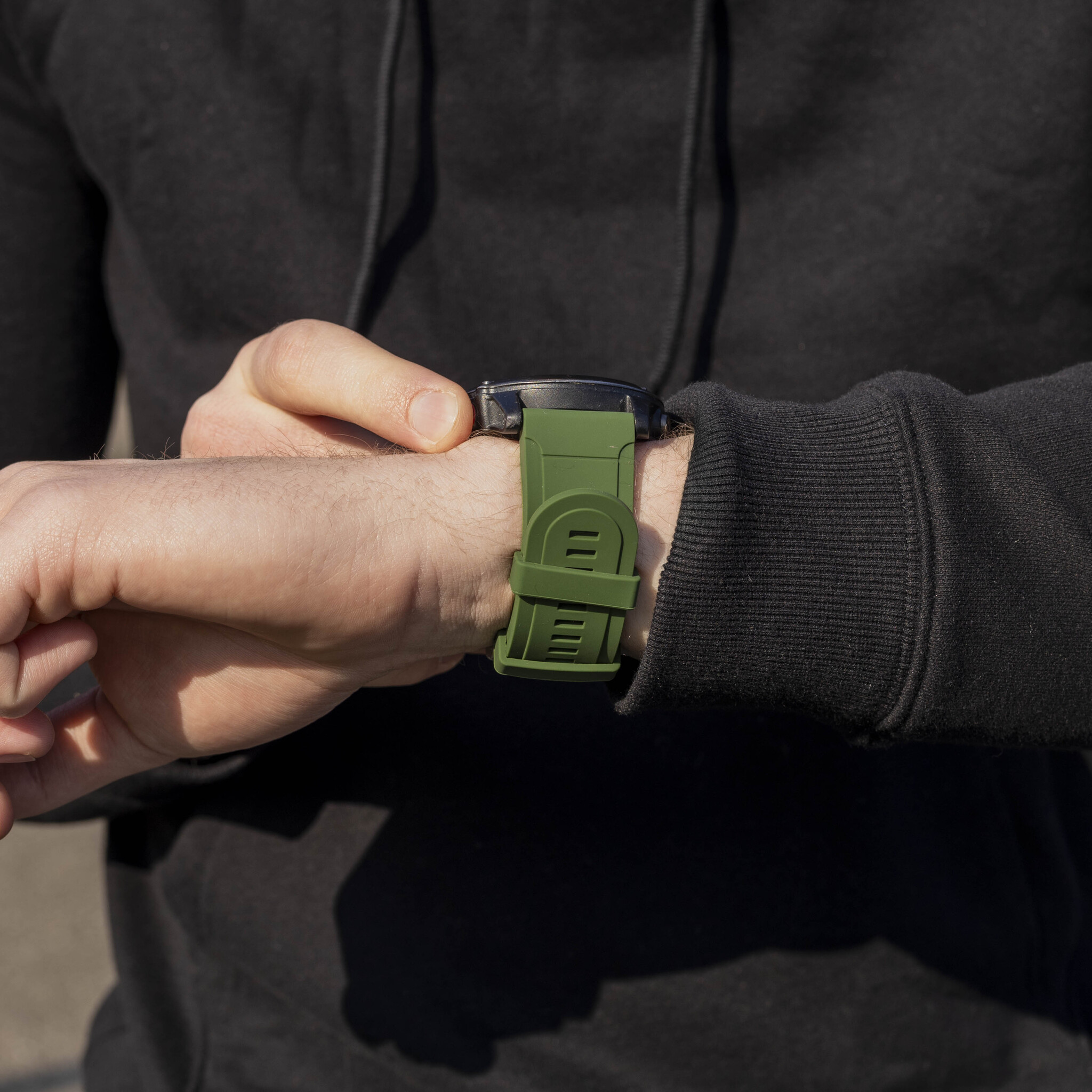Das Handgelenk einer Person mit grünem Armband und schwarzem Zifferblatt.