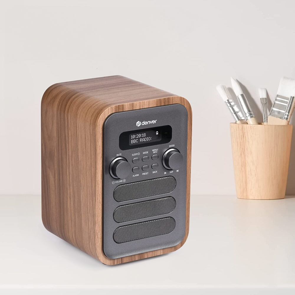 Drewniane radio w kształcie kostki z wyświetlaczem cyfrowym i panelem sterowania, obok materiałów artystycznych.