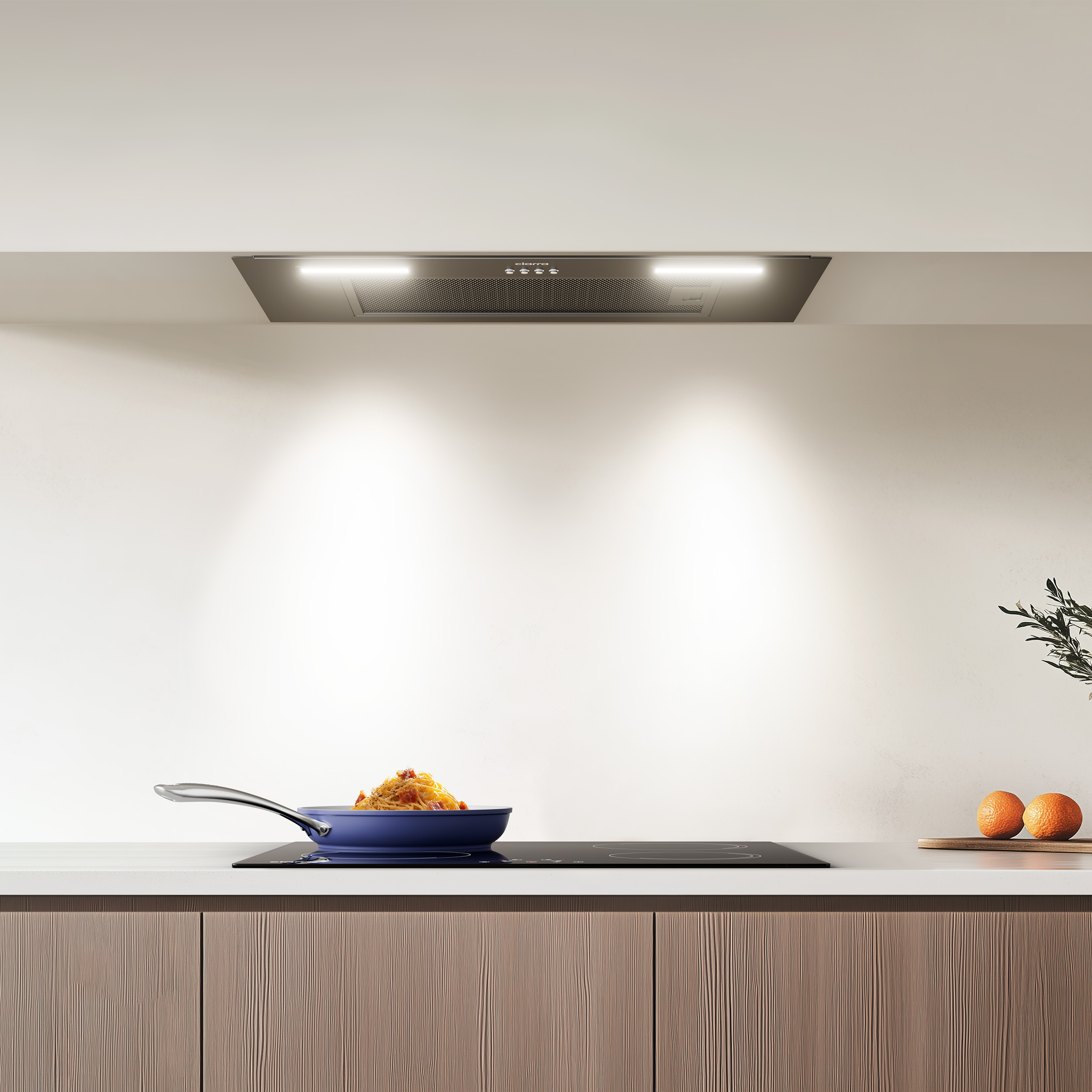Moderne keuken met pan op zwarte kookplaat en afzuigkap; sinaasappels aan de zijkant.