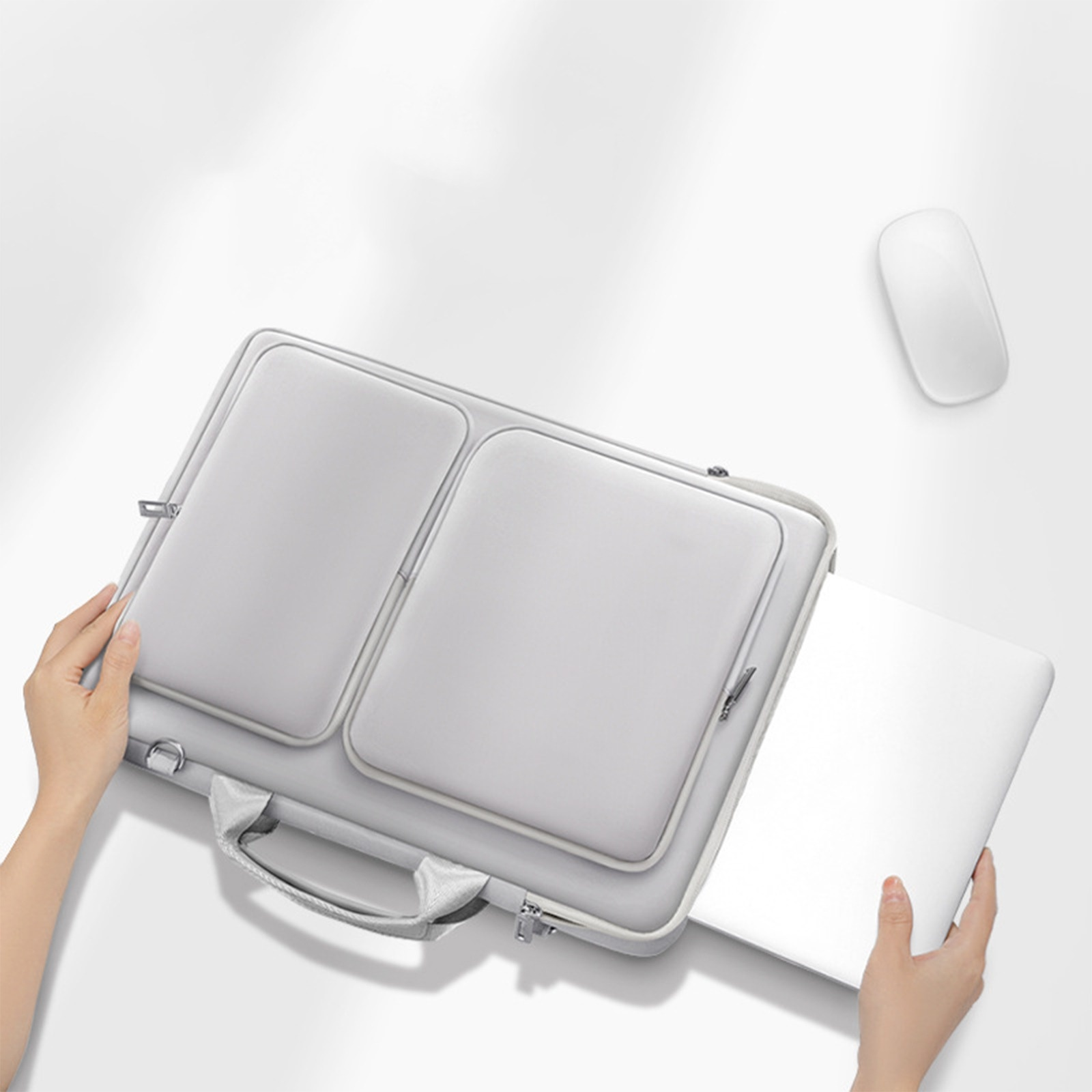 Eine graue Laptoptasche mit einem Laptop darin. In der Nähe befindet sich eine weiße Maus.