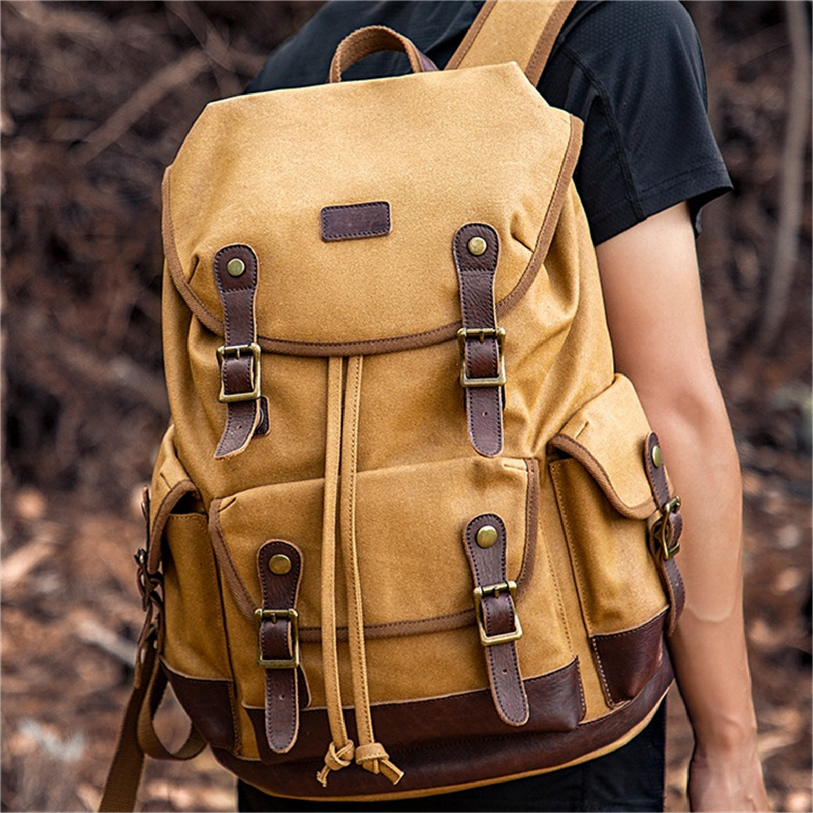 Ein beigefarbener Canvas-Rucksack mit braunen Lederriemen und Akzenten, der von einer Person getragen wird.