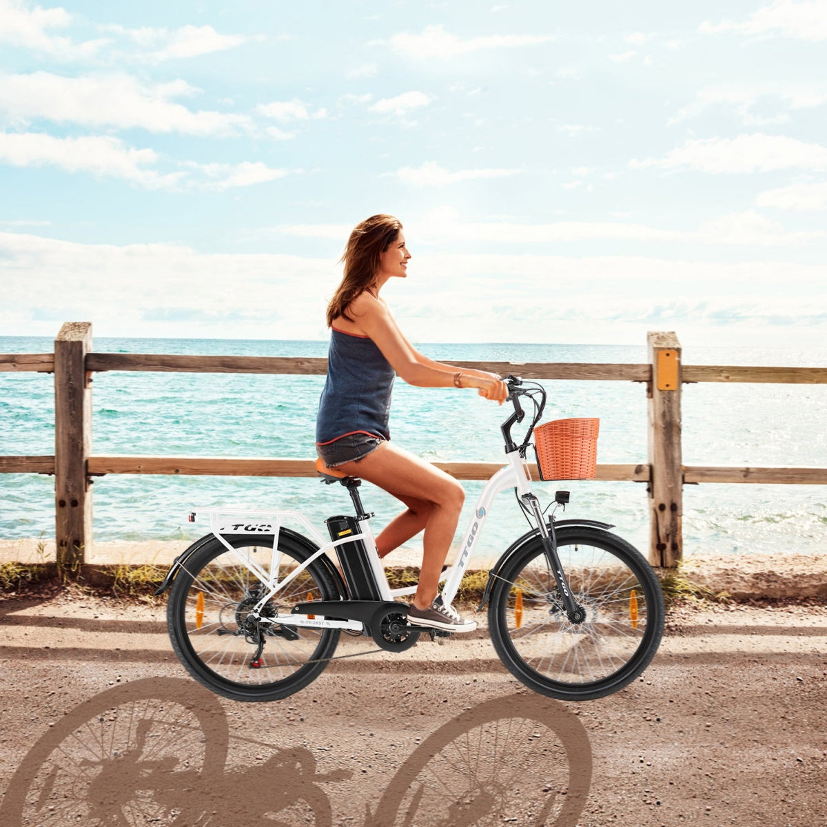 Frau fährt mit weißem E-Bike auf einem Steg am Meer entlang. Korb am Lenker.