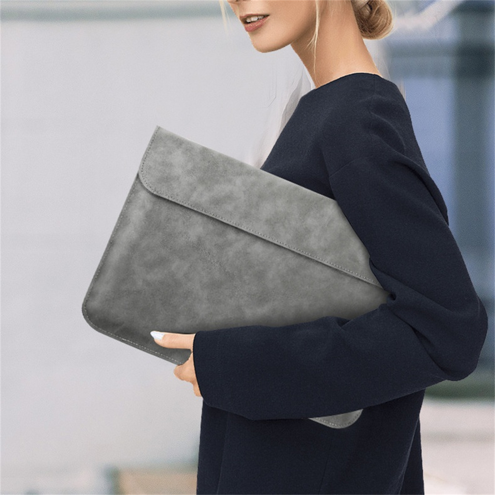 Eine Person, die einen dunklen Pullover trägt, hält eine graue Laptoptasche.