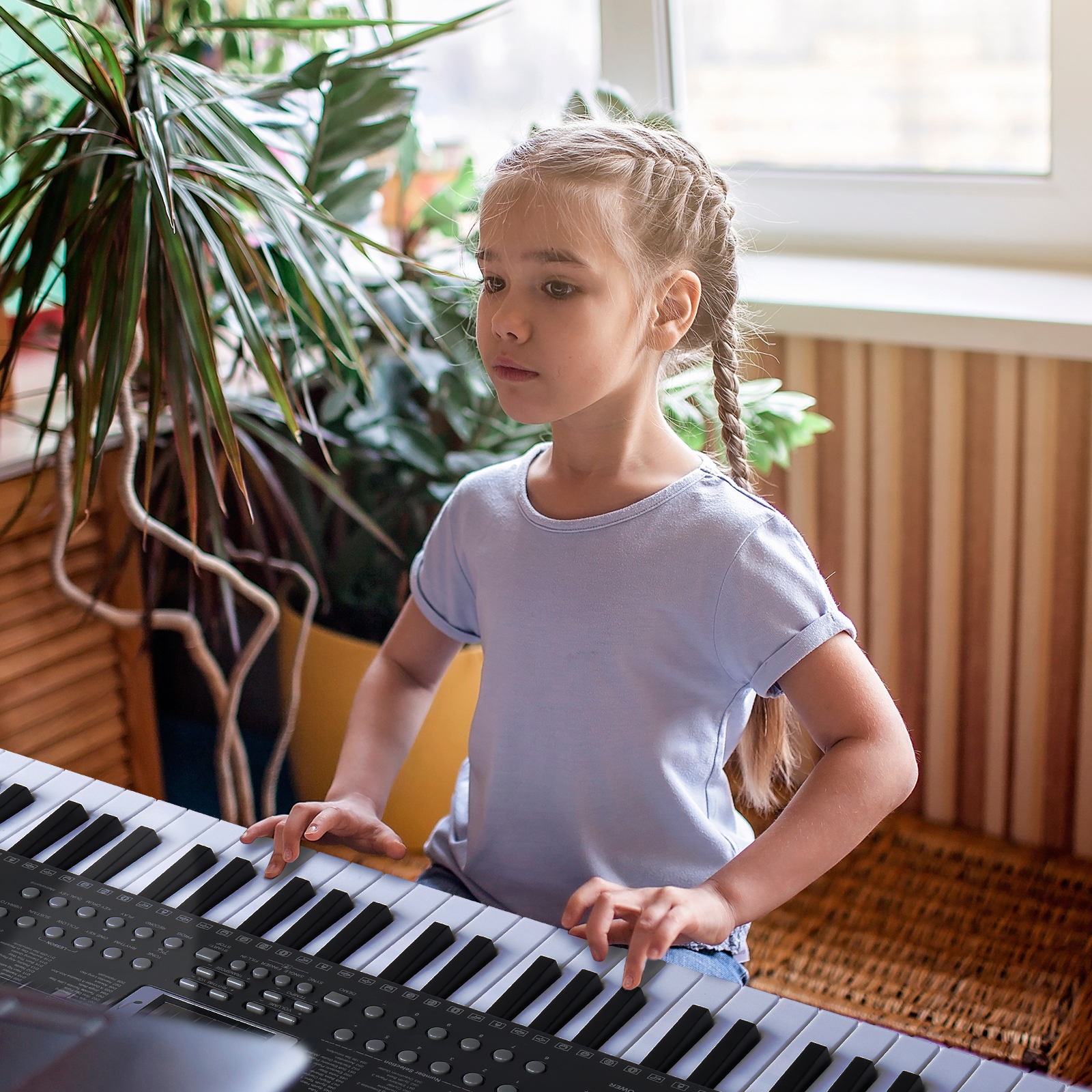 Ein junges Mädchen mit Zöpfen spielt Keyboard. Im Hintergrund ist eine Pflanze zu sehen.