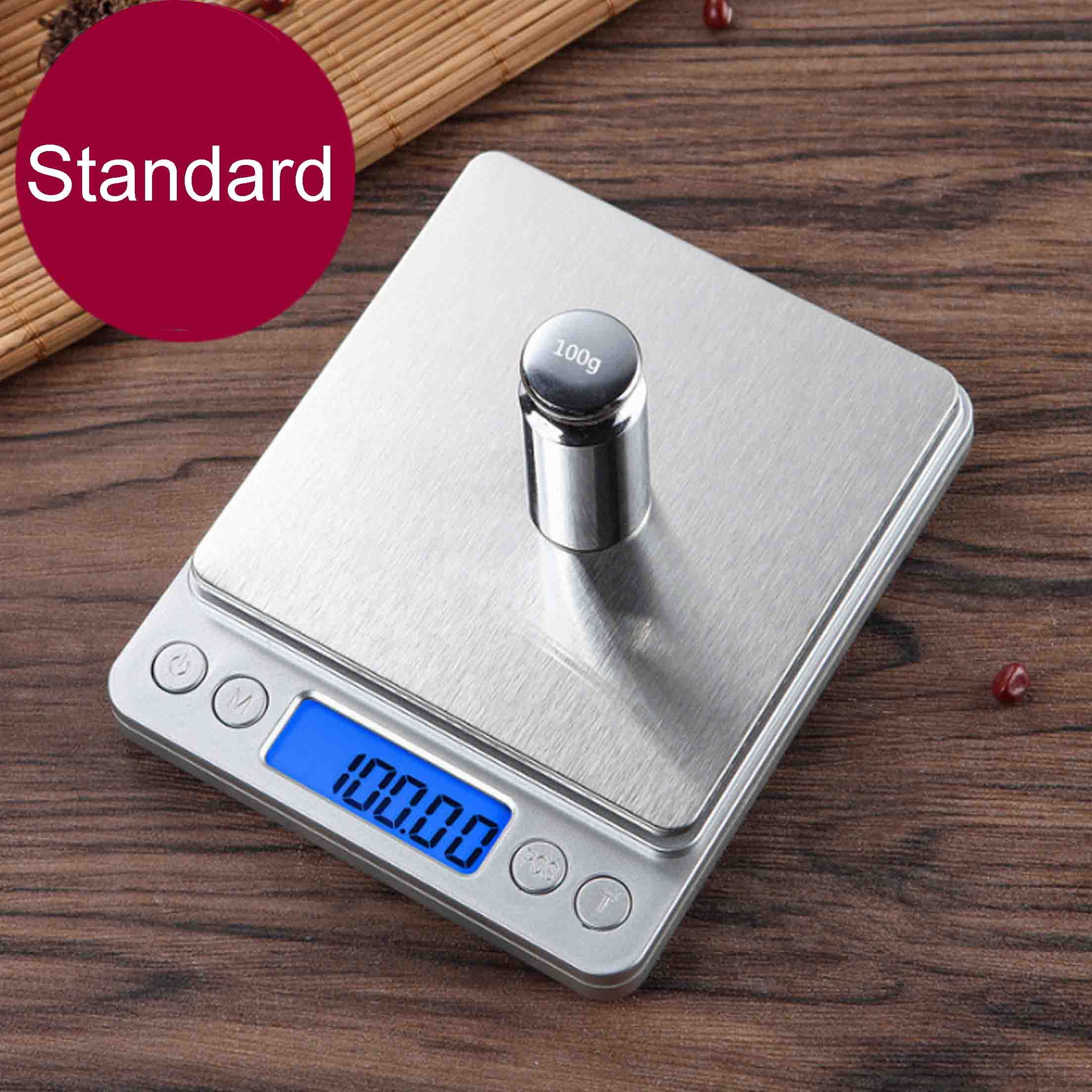 Eine Digitalwaage mit einem 100g Gewicht. Der Bildschirm zeigt 100,00. Ein roter Kreis mit 'Standard' ist sichtbar.