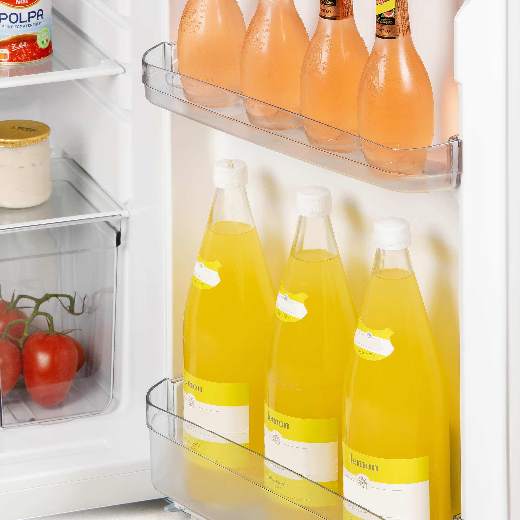 Réfrigérateur ouvert avec plusieurs bouteilles de jus et des tomates.