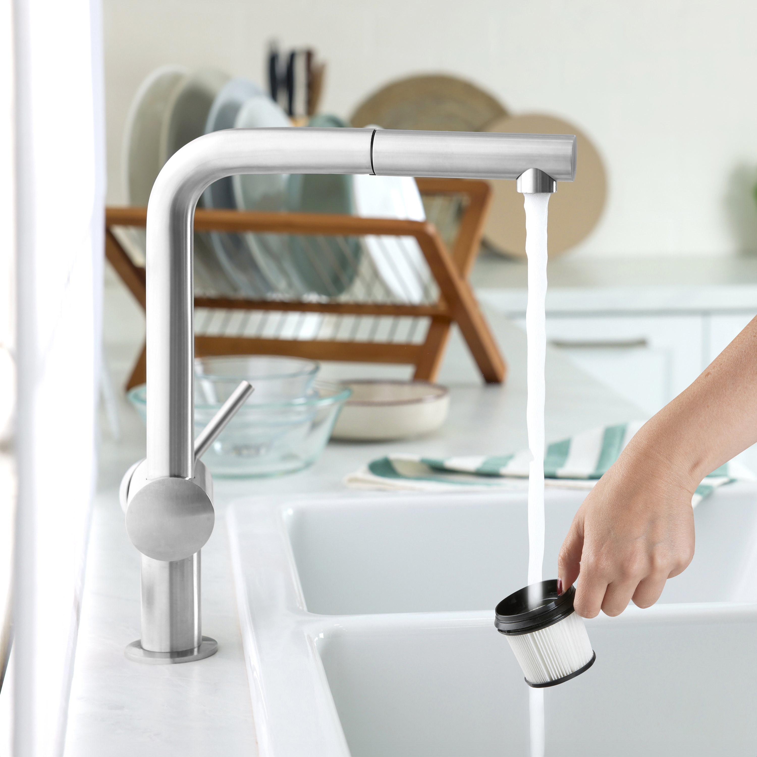 Un robinet avec de l'eau qui coule dans un évier, une personne tient un filtre à vide.