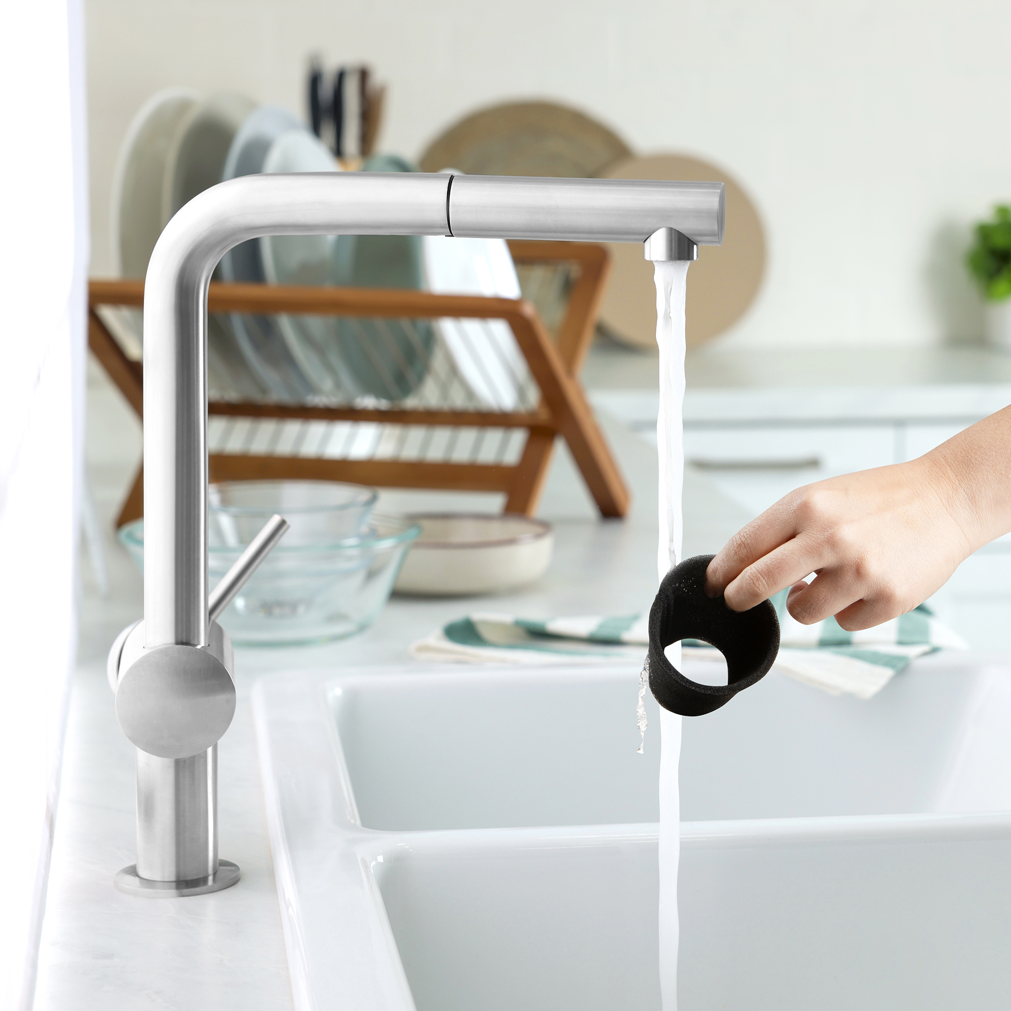 Un robinet avec de l'eau courante et une main tenant une éponge noire en dessous.