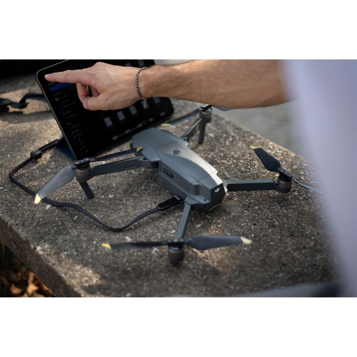 Un drone et une tablette sur une surface en béton. Une main pointe vers l'écran de la tablette.