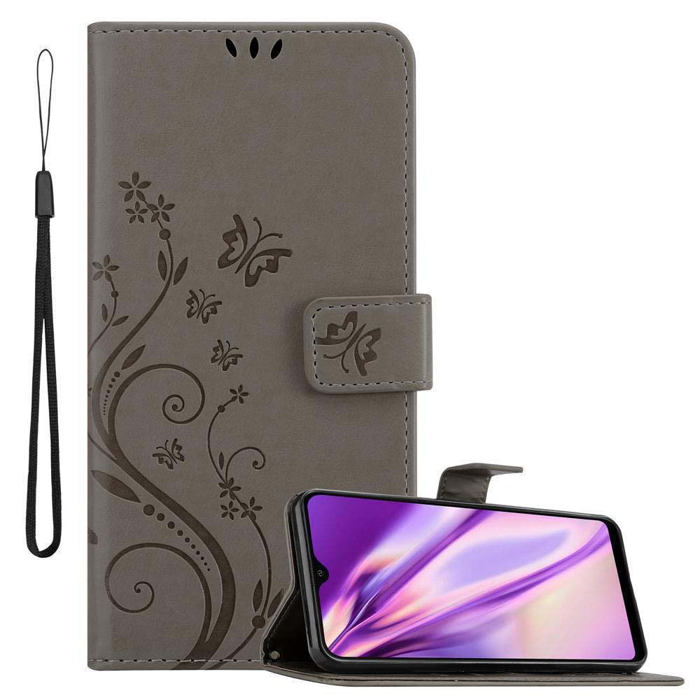 Custodia a portafoglio grigia con design floreale, farfalle e cinturino, che tiene un telefono con schermo viola.