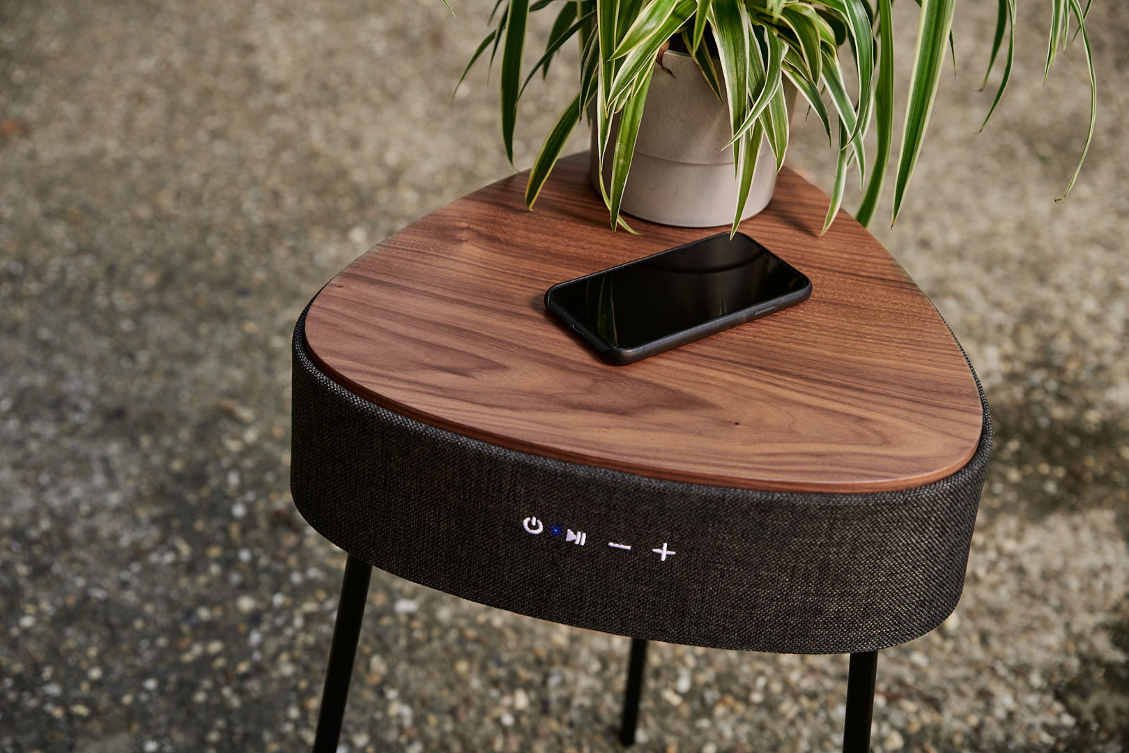 Houten driehoektafel met een smartphone en een plant erop. De tafel heeft een luidspreker en metalen poten.