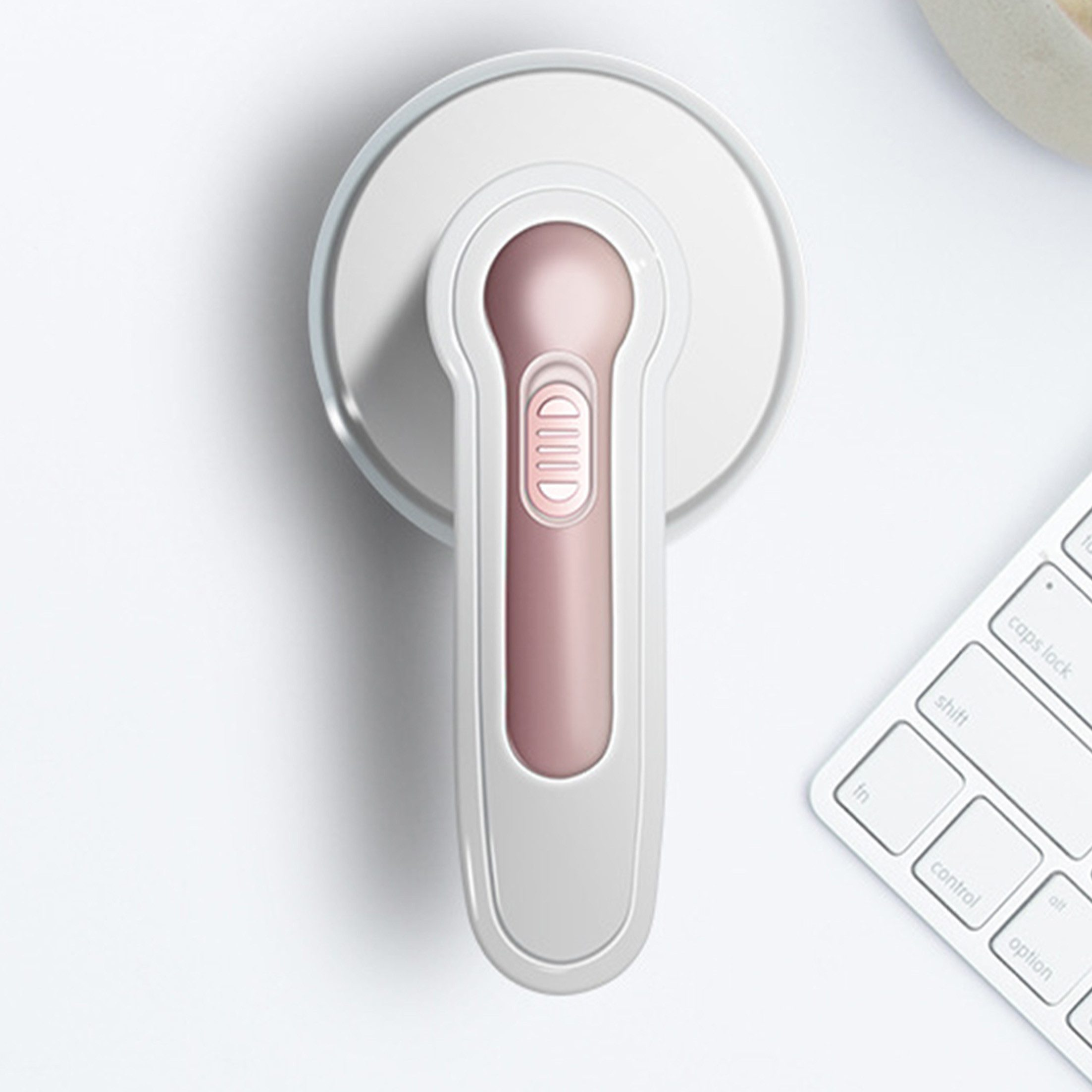 Draufsicht auf ein weißes und rosa Massagegerät auf einer weißen Oberfläche neben einer Tastatur.