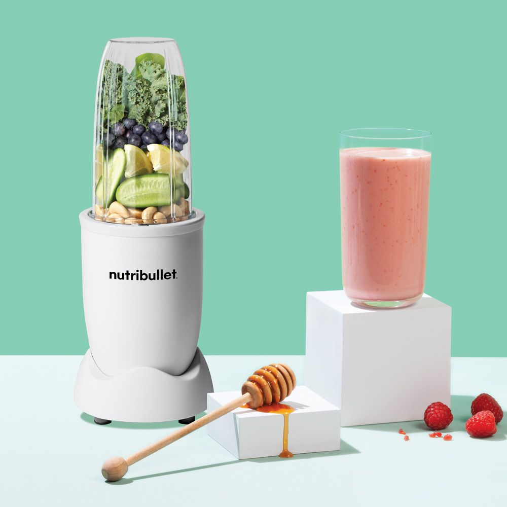 Een witte blender met een glas roze smoothie en een honingdipper, en een glas smoothie.
