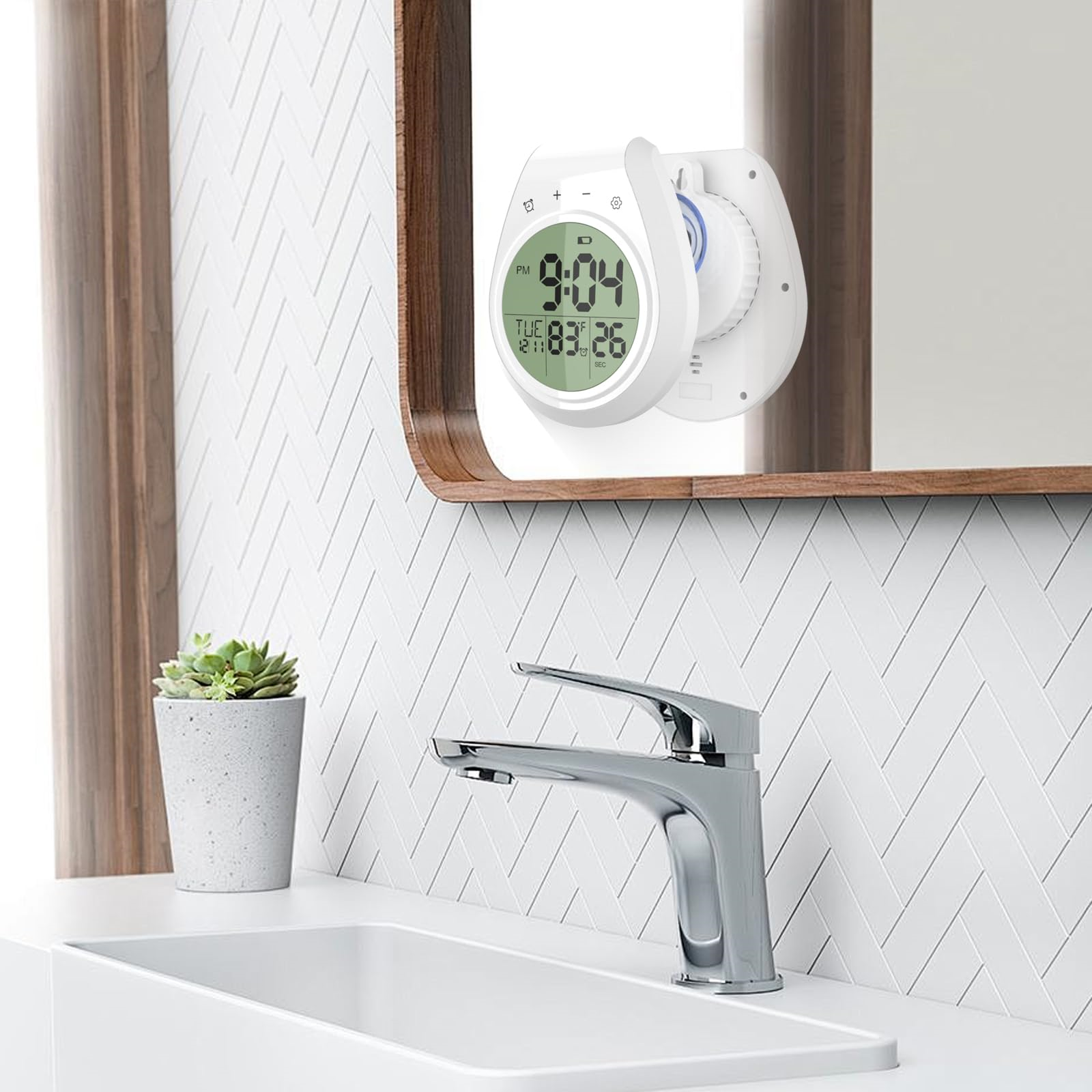 Eine Digitaluhr ist über einem Waschbecken an einem Spiegel befestigt. Eine kleine Pflanze steht neben dem Wasserhahn.