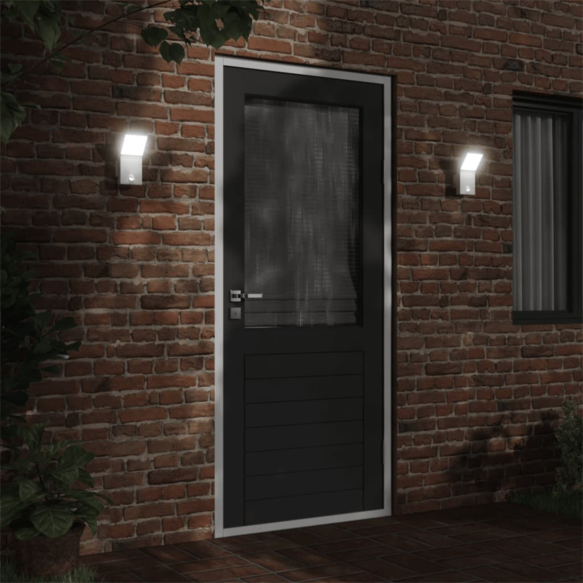 Ziegelmauer mit einer schwarzen Tür. Zwei Lichter sind an der Seite angebracht. Ein Fenster ist ebenfalls sichtbar.