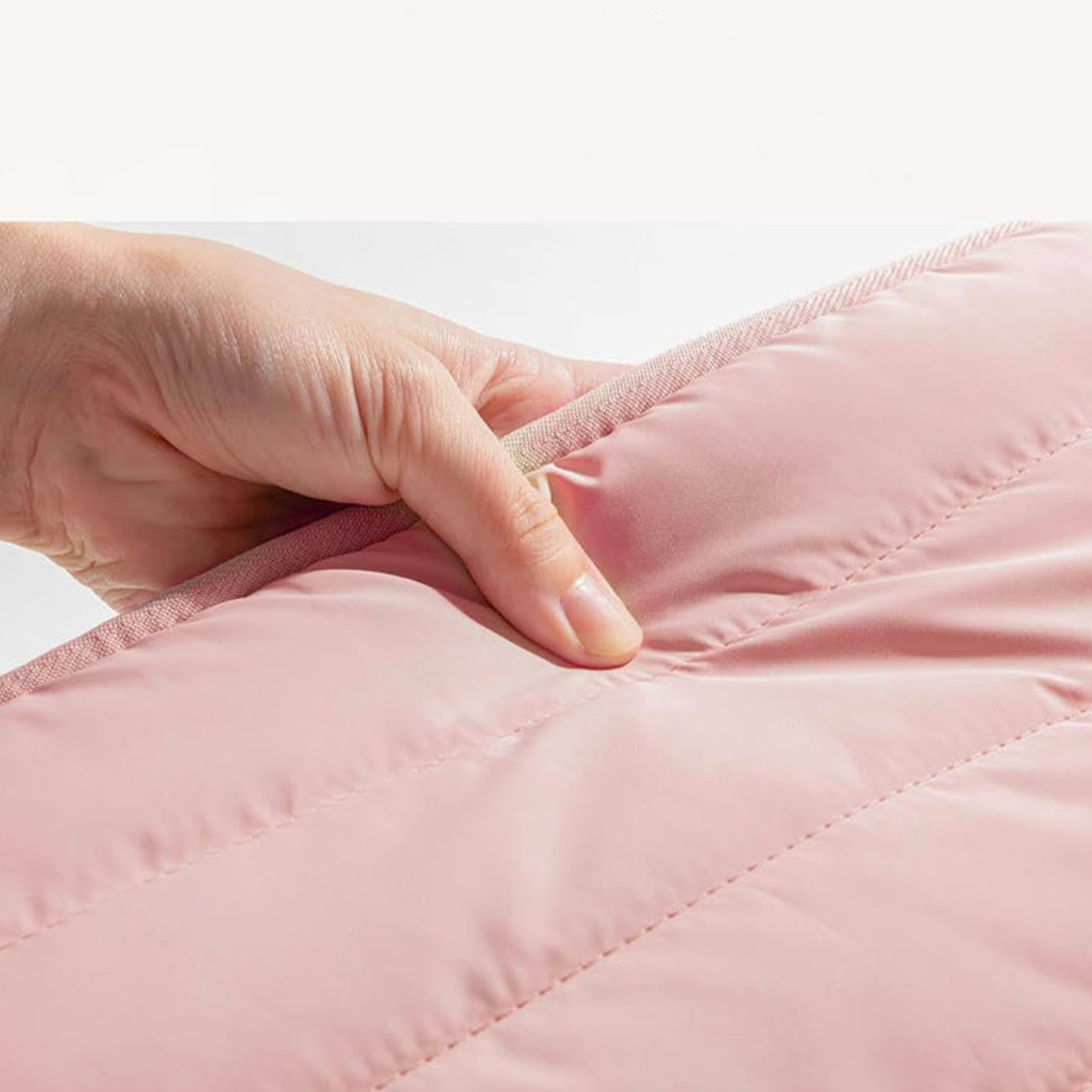 Eine Hand berührt eine rosa gesteppte Oberfläche, was Weichheit und Textur anzeigt.