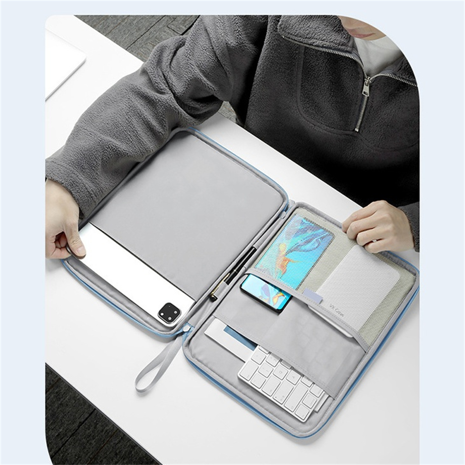 Person öffnet eine blaue Reißverschluss-Tasche. Inhalt: Tablet, Telefon, Stift, Tastatur, Zubehör.