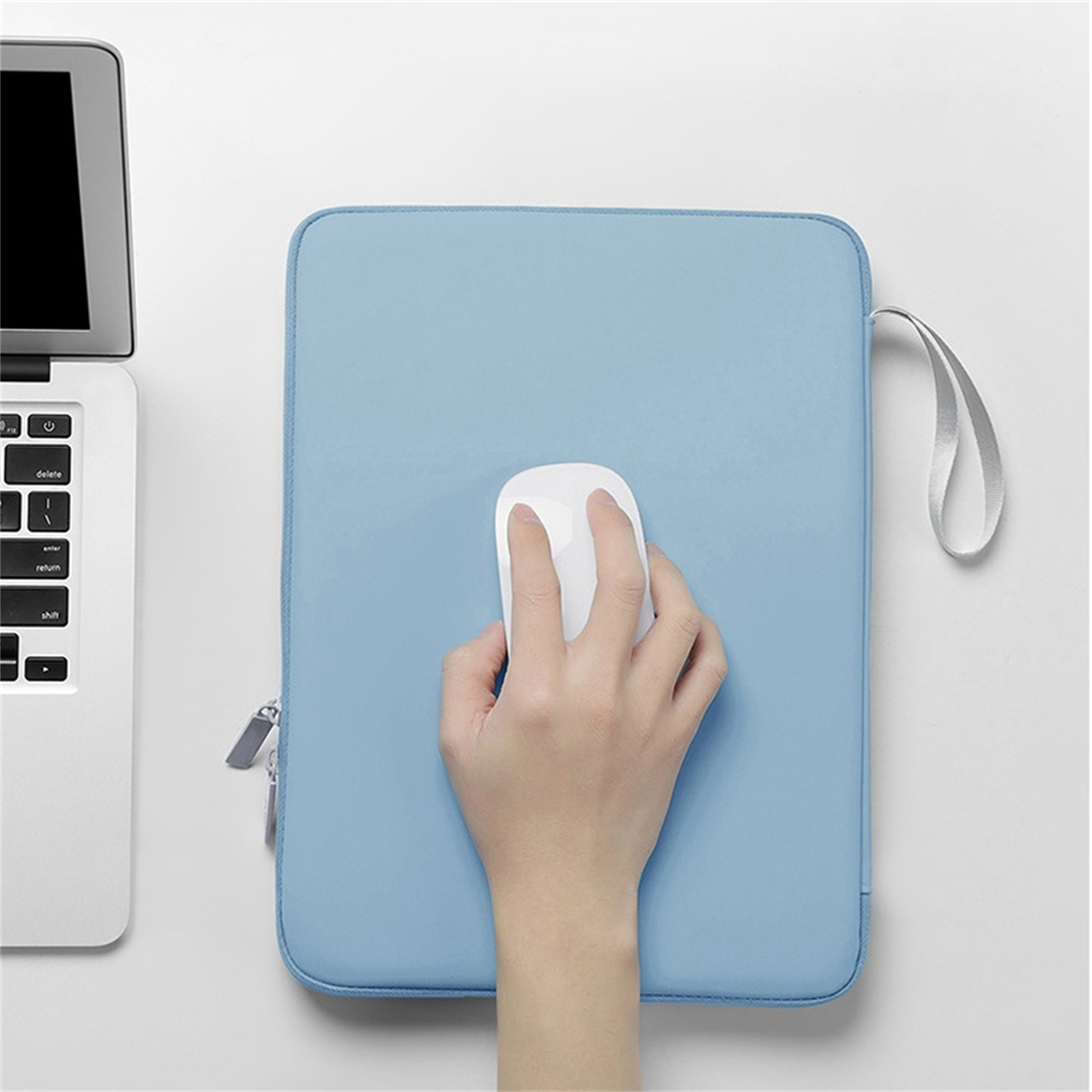 Die Hand einer Person, die eine weiße Maus auf einer hellblauen Laptop-Hülle neben einem Laptop benutzt.