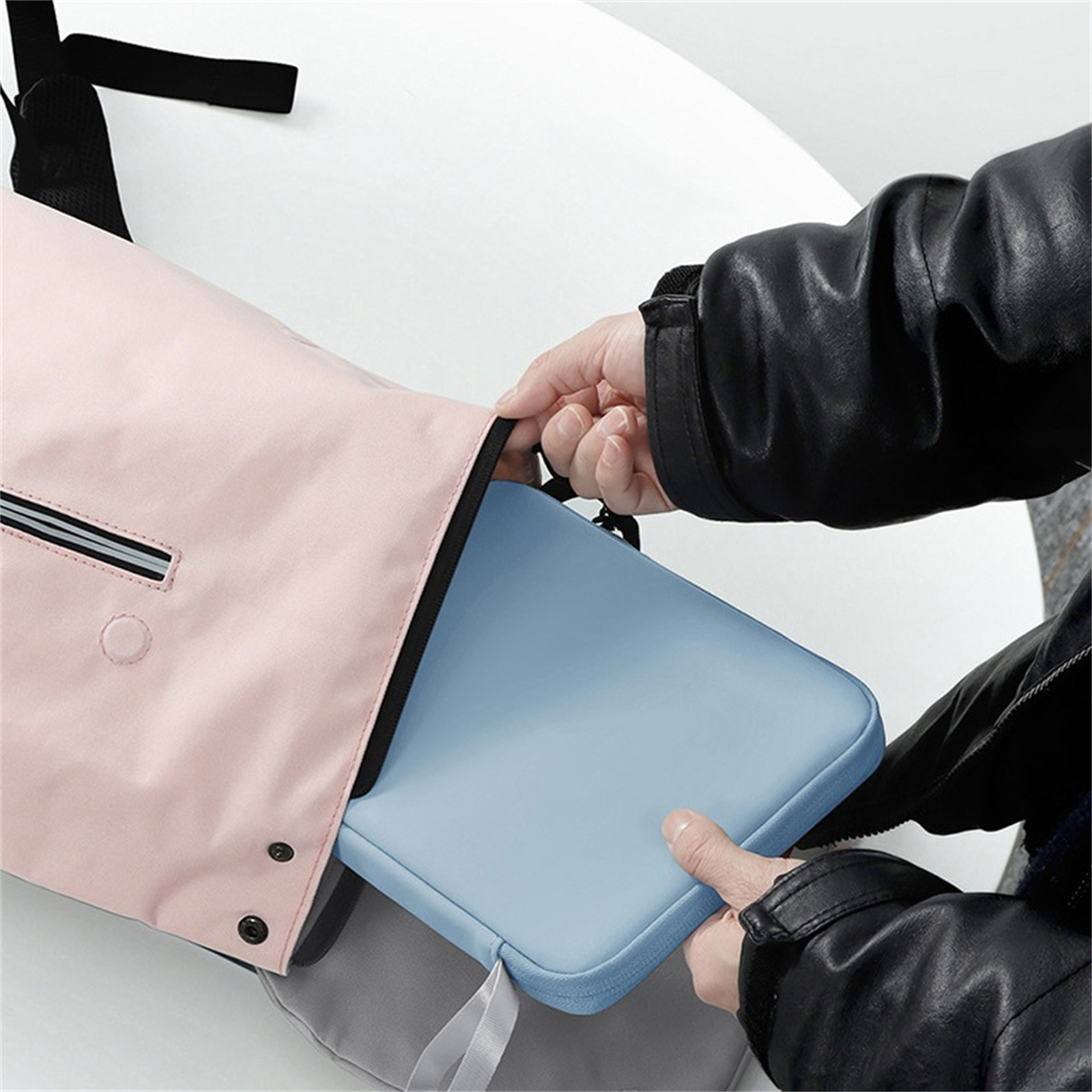 Hände legen einen hellblauen Laptop in eine rosa Tasche auf einen weißen Tisch.