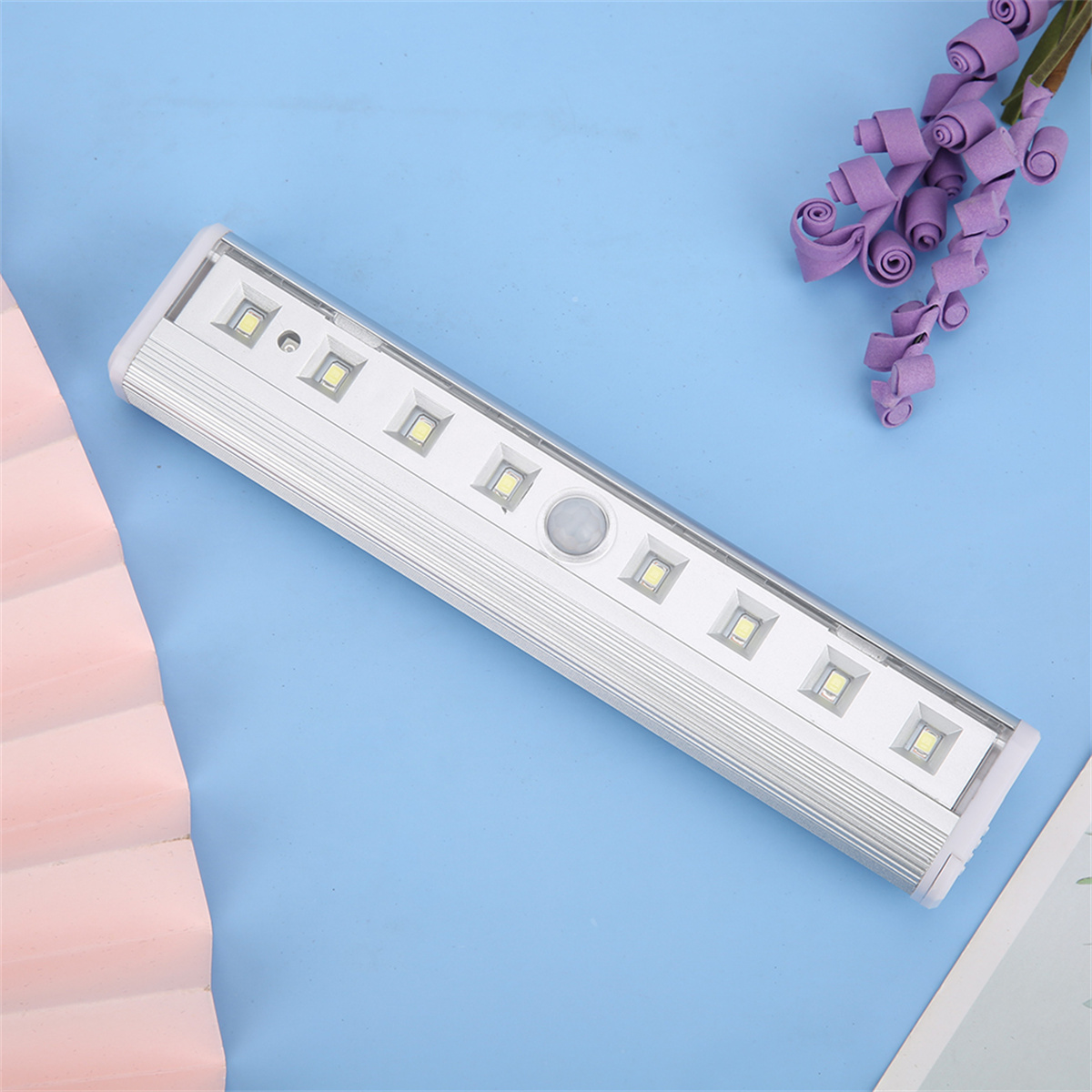 Silberne LED-Lichtleiste mit Bewegungssensor und LEDs auf blauer Oberfläche.