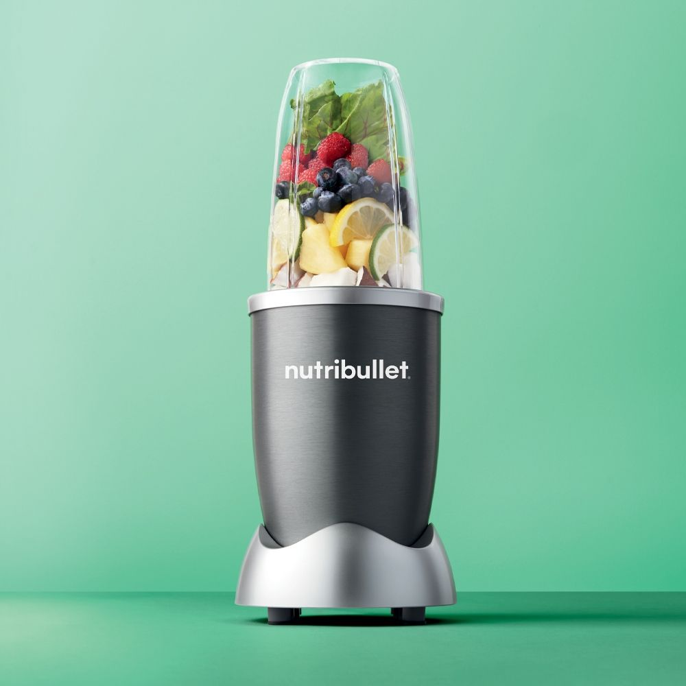 Nutribullet blender met fruit. Grijze basis, doorzichtige container gevuld met fruit en groenten.