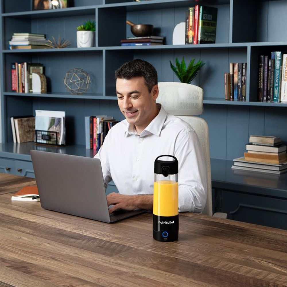 Man werkt op een laptop met een nutribullet blender naast hem.