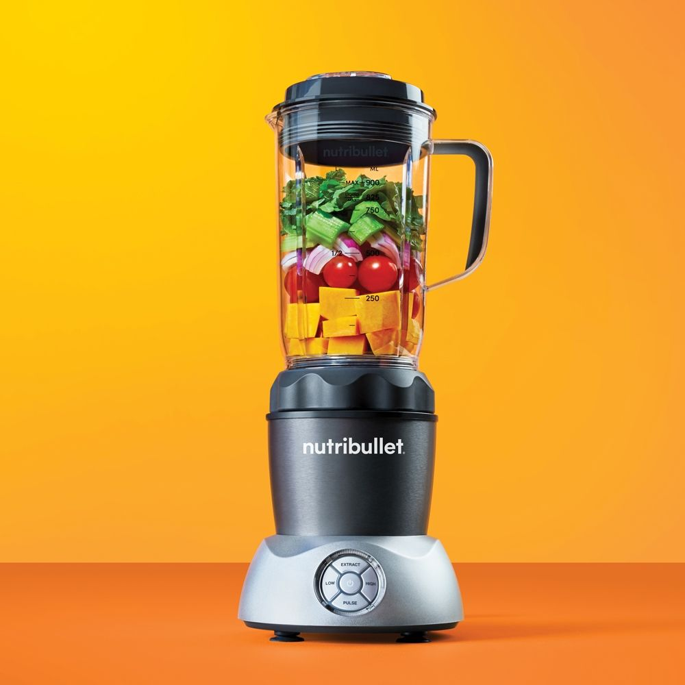Nutribullet blender met gesneden groenten erin, oranje achtergrond.