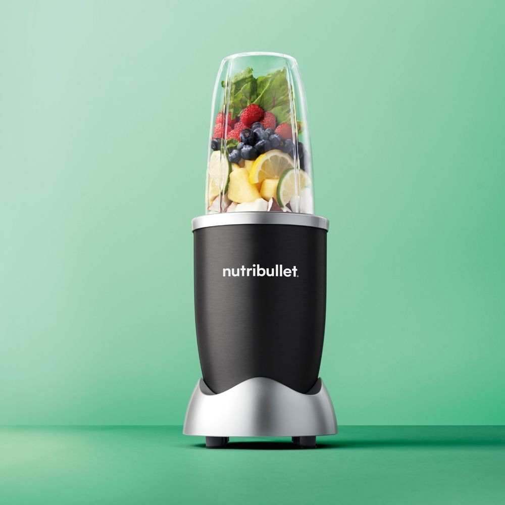 Blender Nutribullet avec fruits à l'intérieur. Base noire et récipient transparent. Fond vert.