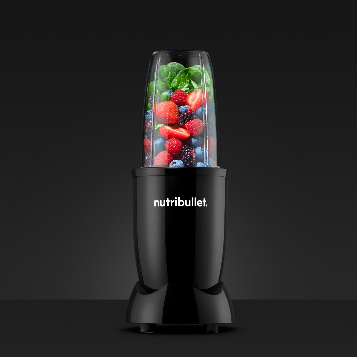 Een zwarte Nutribullet-blender met verse bessen erin, tegen een donkere achtergrond.