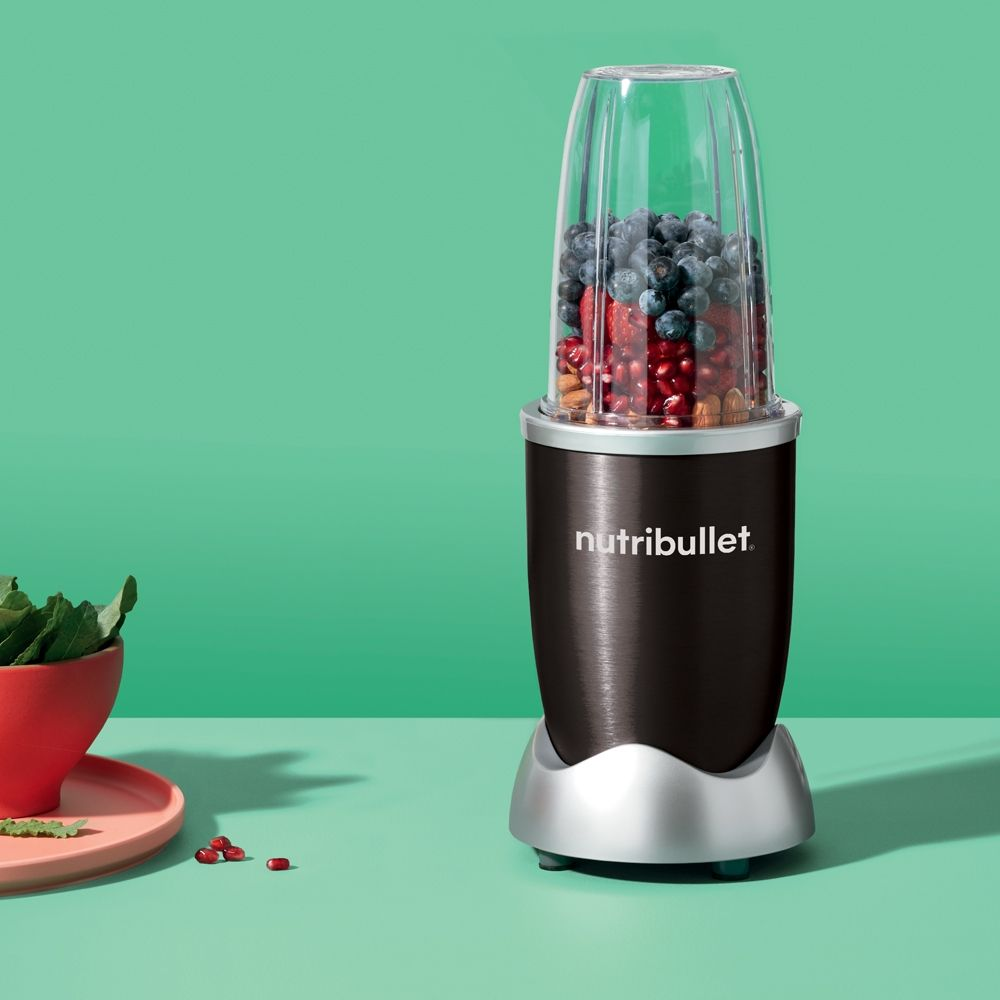 Un blender Nutribullet avec un récipient rempli de fruits sur une surface verte.
