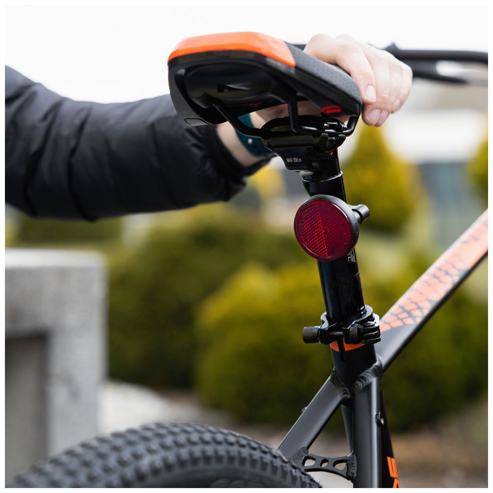 Die Hand einer Person, die einen Fahrradsattel hält. Ein roter Reflektor ist an der Sattelstütze befestigt.
