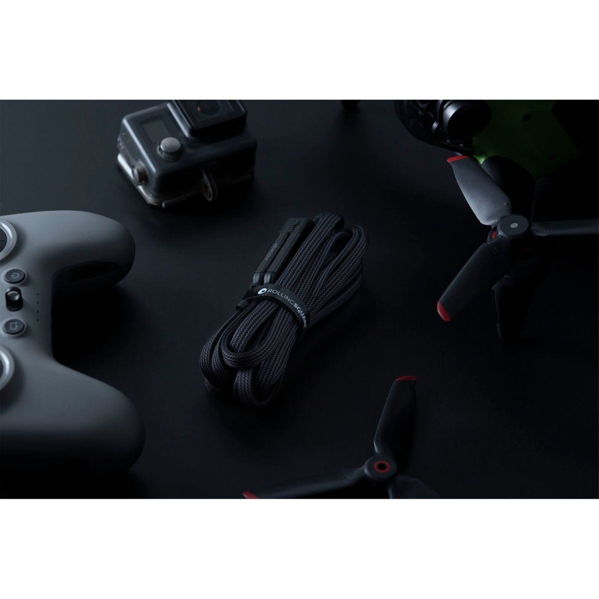 Accessoires de drone noirs sur une surface noire : contrôleur, hélices et câble avec une sangle.