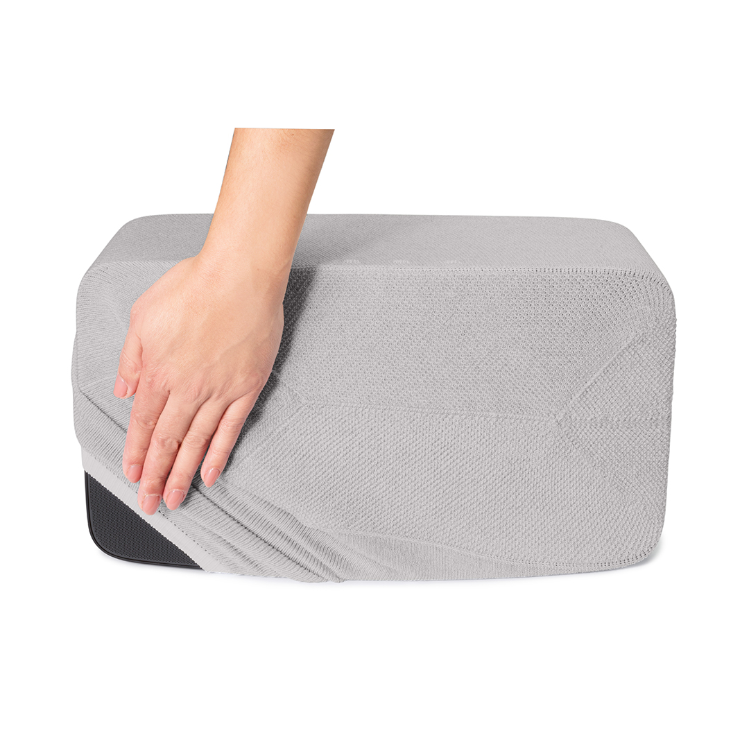 Une main tire une housse grise texturée sur une boîte noire rectangulaire. La housse est tendue.