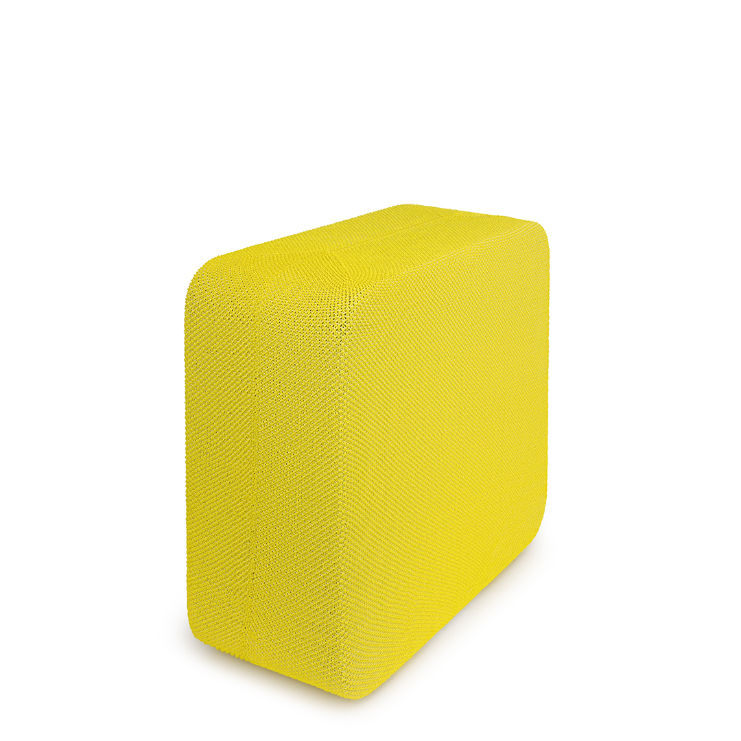 Un cube rectangulaire jaune, posé sur une surface blanche. Le cube a une surface texturée.