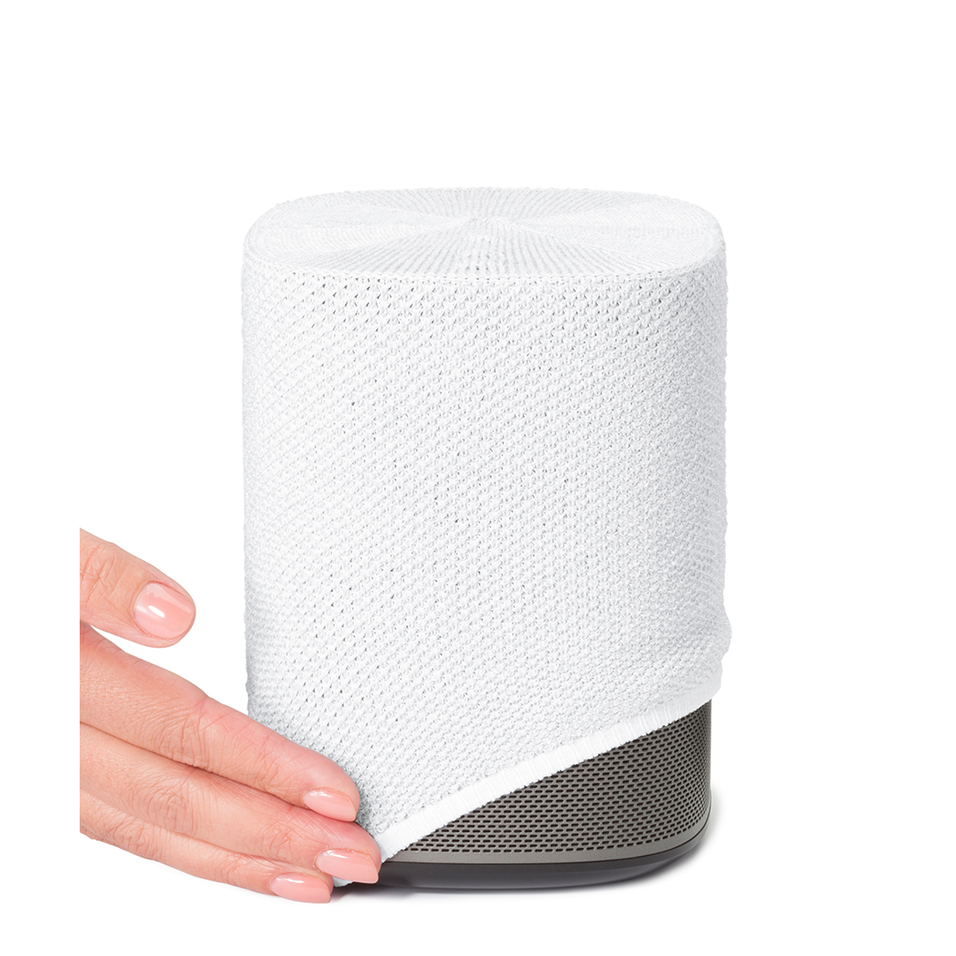 Un haut-parleur blanc partiellement recouvert d'une housse en tricot blanc. Une main tient la housse.