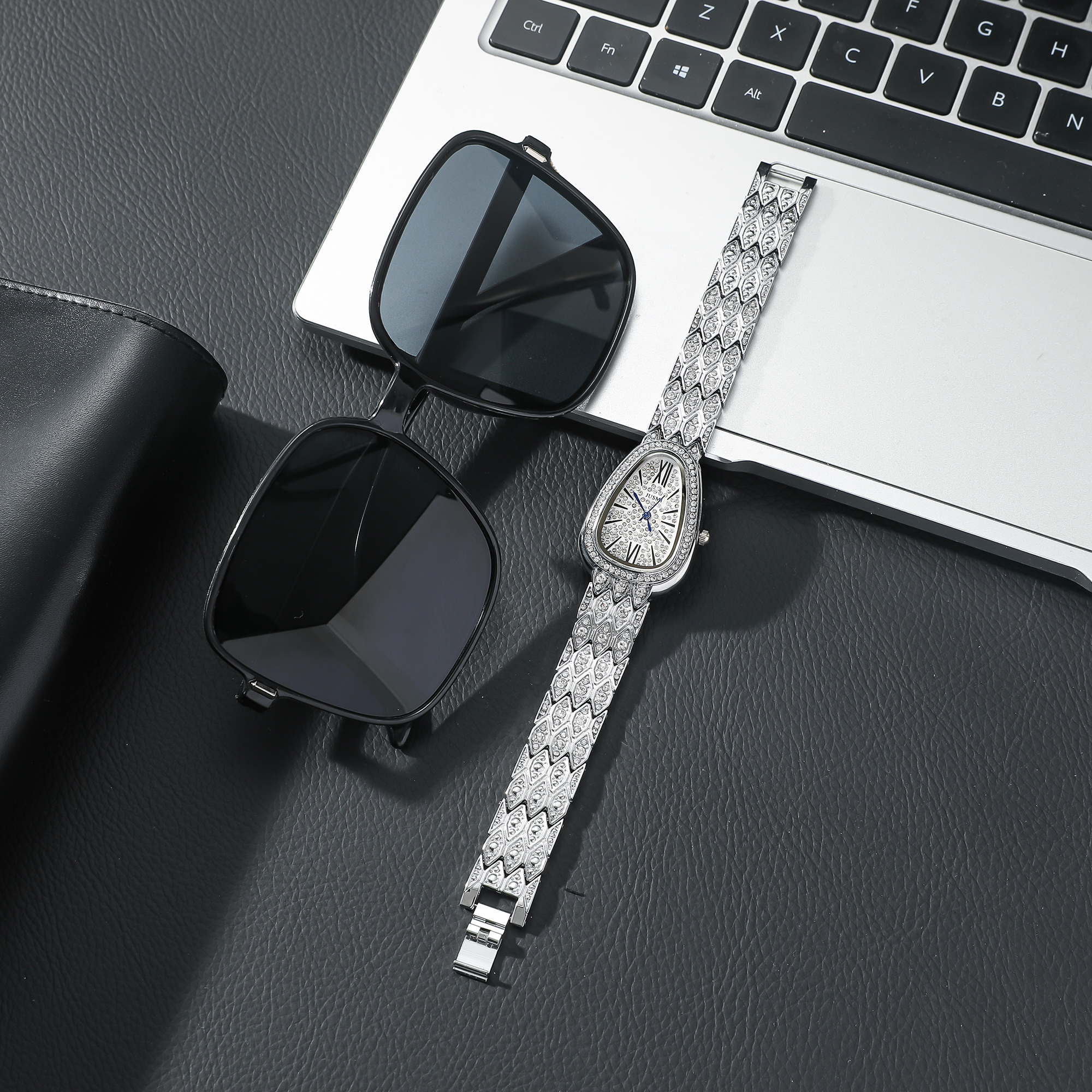 Sonnenbrille und Armbanduhr auf schwarzer Oberfläche. Ein Laptop ist im Hintergrund sichtbar.