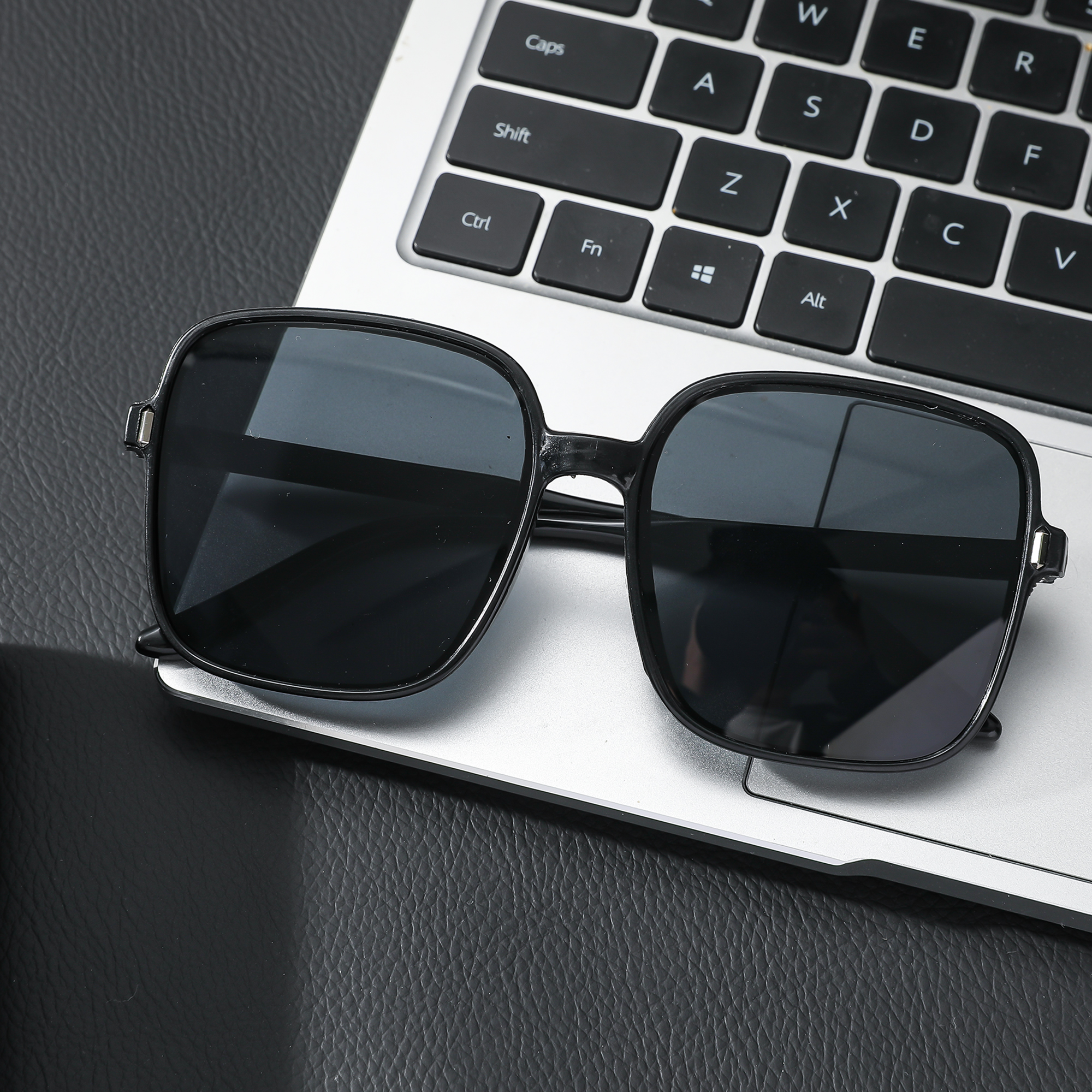 Schwarze quadratische Sonnenbrille auf einer Laptop-Tastatur. Die Tastatur ist silber und schwarz.